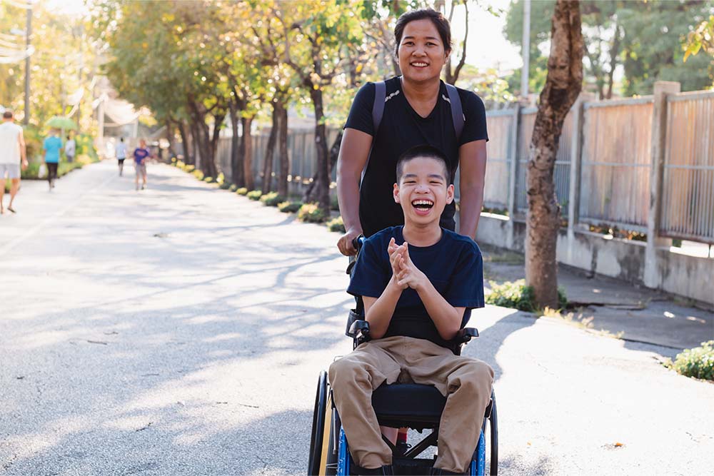 adult push wheelchair of smiling youth. enjoying time in the park.